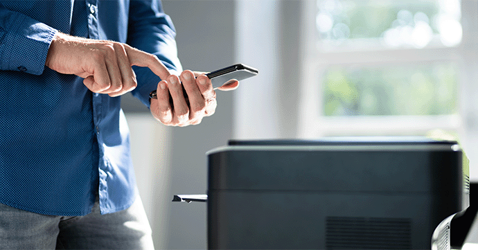 Person holding a smartphone by a printer.