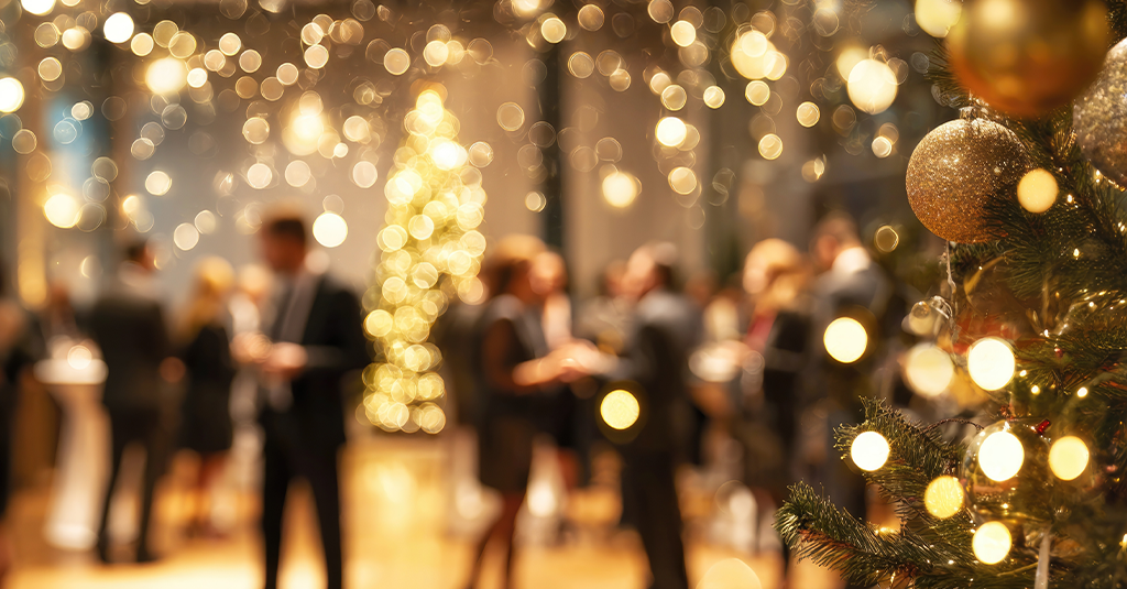 Warmly lit room with a Christmas tree and blurred background of partygoers in formal wear.