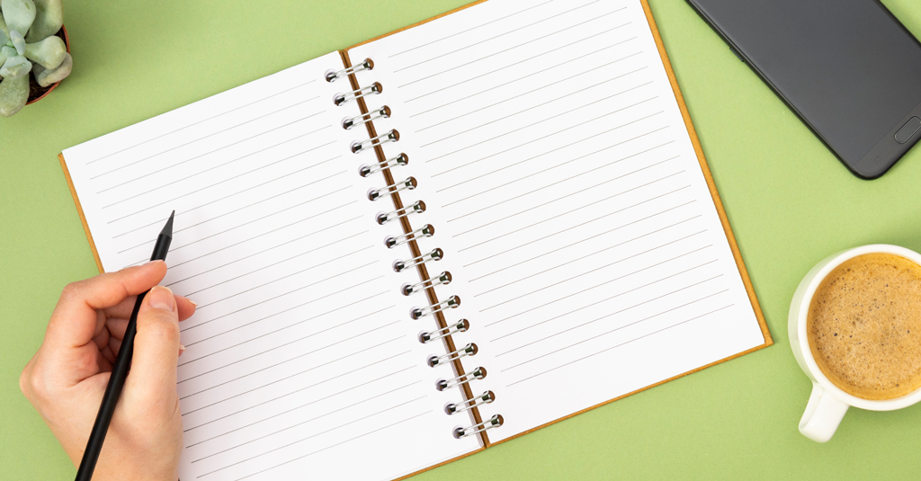 Lined Notebooks An open, lined notebook and a hand holding a pen.