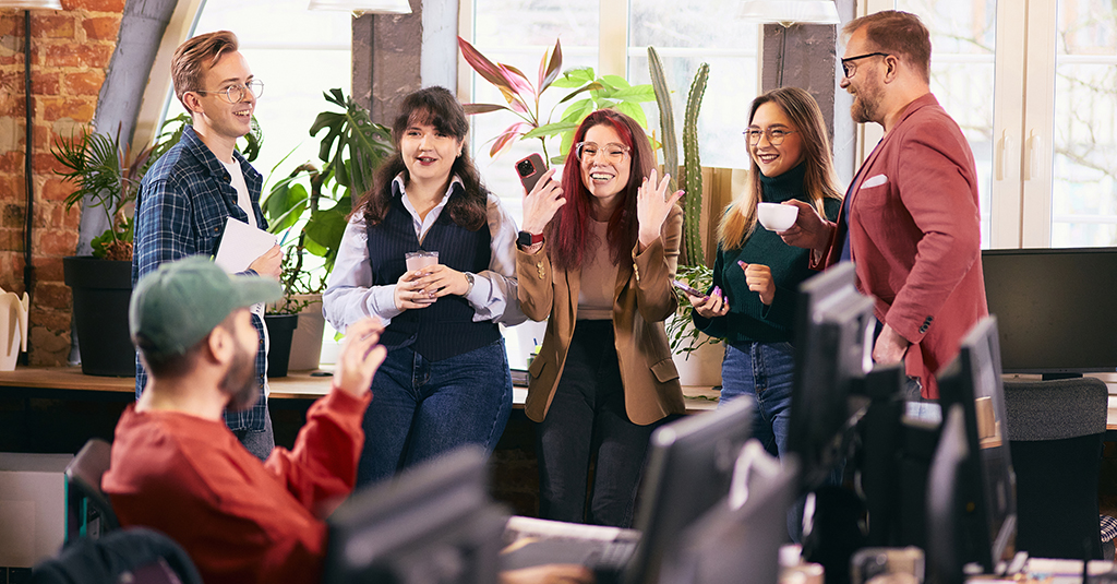 Chatty colleagues standing around office worker at desk